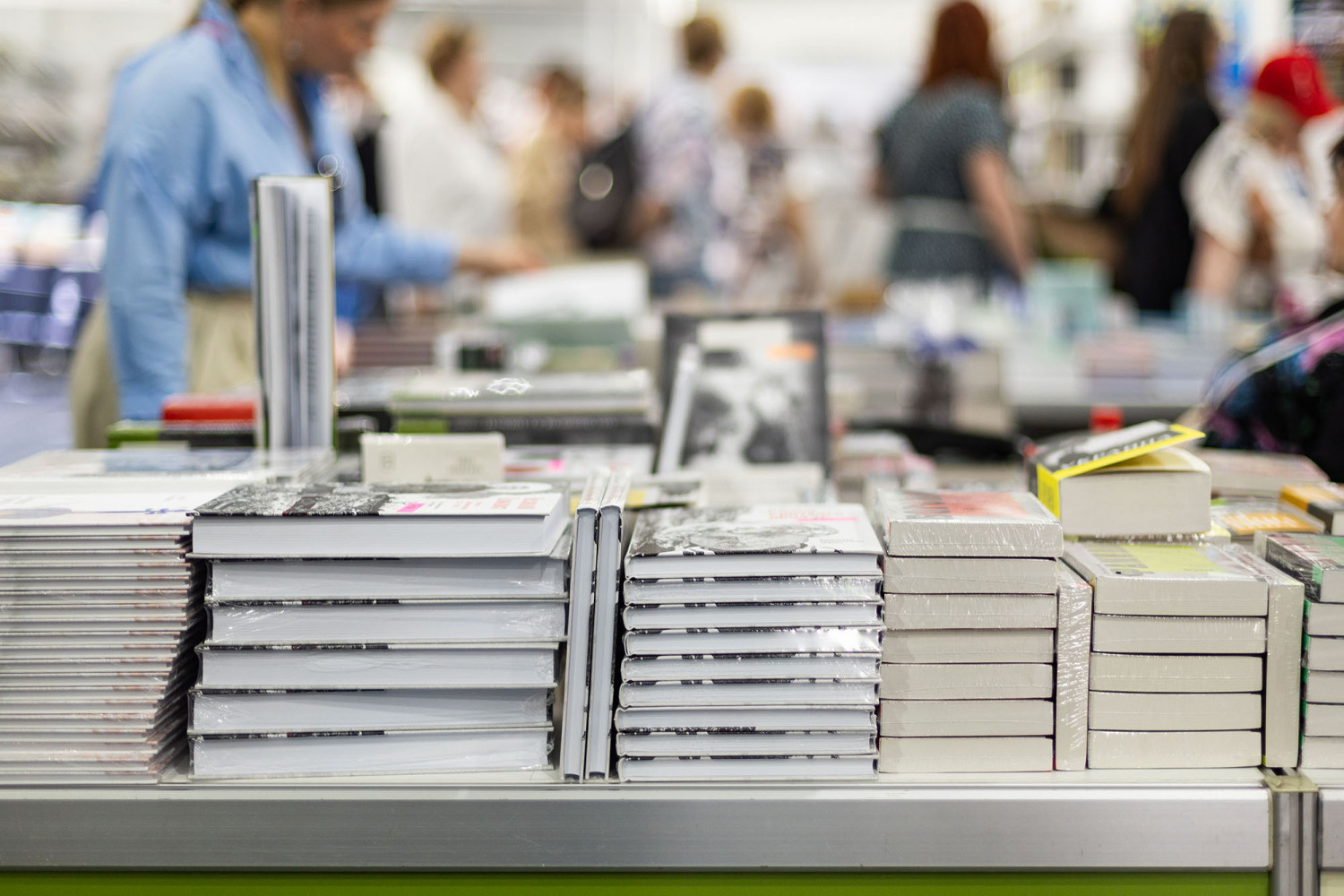 Bücherstapel auf einem Tisch mit Menschen im Hintergrund